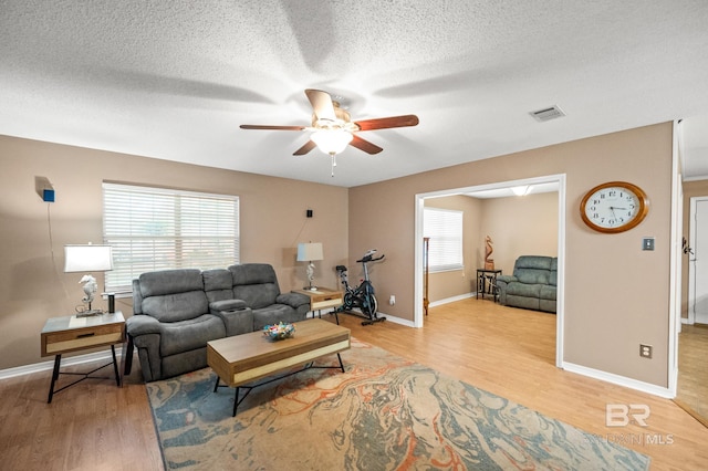 living room featuring ceiling fan, a textured ceiling, and light wood-type flooring