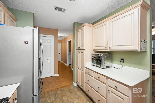 kitchen featuring range, stainless steel fridge, a textured ceiling, and light brown cabinets