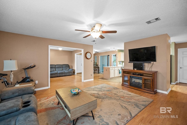 living room with ceiling fan, light hardwood / wood-style floors, and a textured ceiling