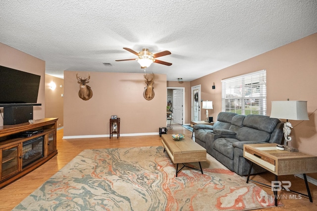 living room featuring ceiling fan, light hardwood / wood-style flooring, and a textured ceiling