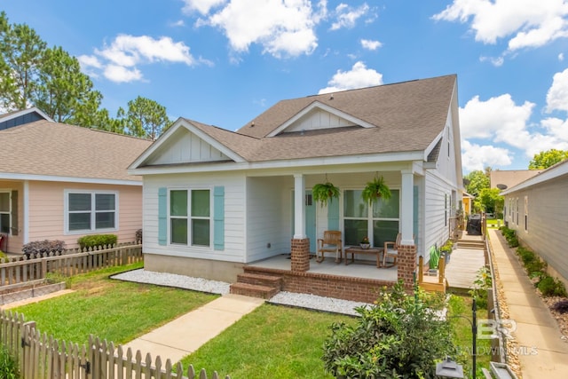 view of front of home with a shingled roof, covered porch, fence, board and batten siding, and a front yard