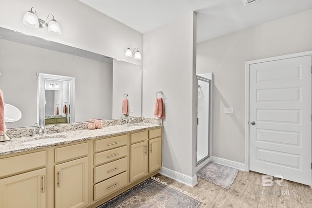 full bath featuring double vanity, a shower stall, a sink, and wood finished floors