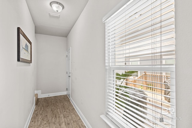 corridor with baseboards, visible vents, and wood finished floors