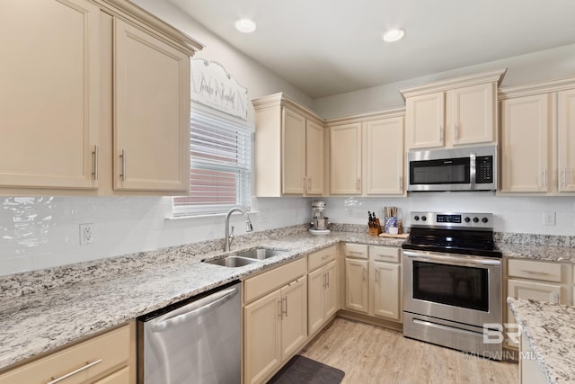 kitchen featuring light stone countertops, cream cabinets, stainless steel appliances, light wood-type flooring, and a sink