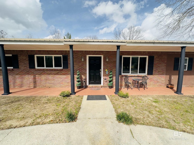 view of front of house with a porch, brick siding, and metal roof