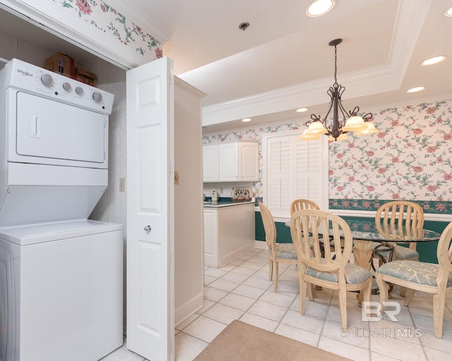 dining space with a tray ceiling, stacked washing maching and dryer, a notable chandelier, light tile floors, and ornamental molding