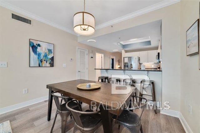 dining area featuring ornamental molding, a tray ceiling, light wood-type flooring, and visible vents