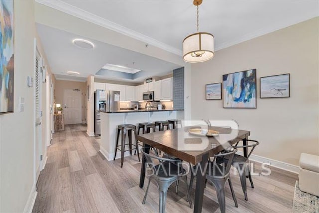 dining room with light wood-style flooring, a tray ceiling, baseboards, and ornamental molding