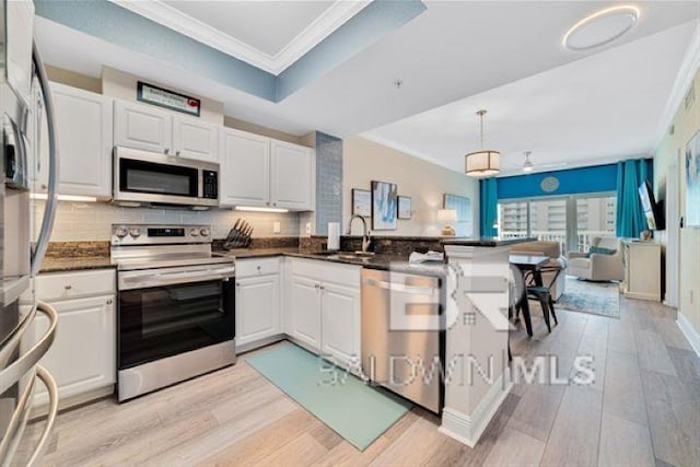 kitchen with a peninsula, a sink, appliances with stainless steel finishes, light wood-type flooring, and crown molding