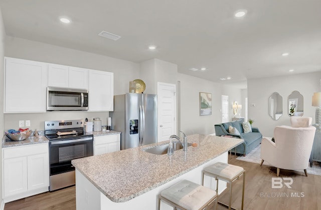 kitchen featuring appliances with stainless steel finishes, a kitchen breakfast bar, a center island with sink, light hardwood / wood-style floors, and white cabinetry