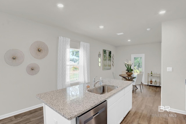 kitchen with stainless steel dishwasher, sink, hardwood / wood-style flooring, white cabinets, and an island with sink