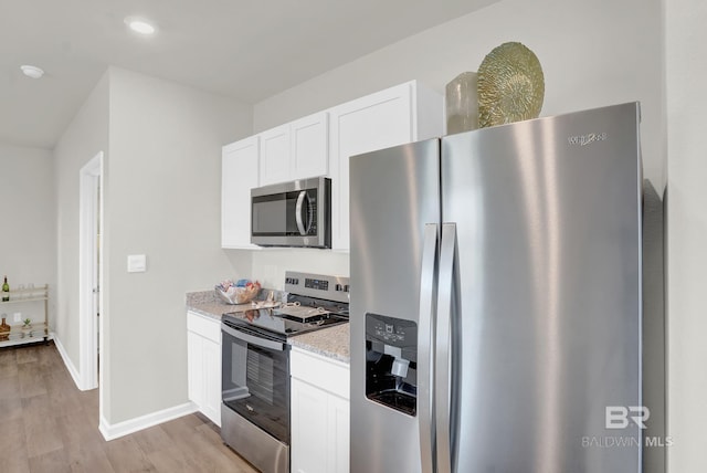 kitchen with light stone counters, white cabinets, stainless steel appliances, and light wood-type flooring