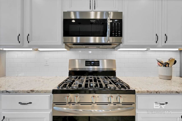 kitchen with stainless steel appliances, white cabinetry, light stone counters, and tasteful backsplash