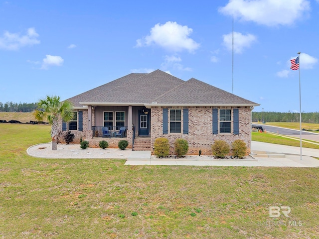 view of front of property featuring a front yard, covered porch, brick siding, and roof with shingles