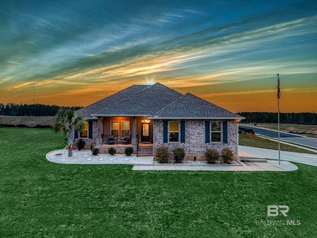 view of front of property with covered porch, roof with shingles, a yard, and brick siding