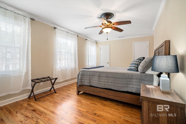 bedroom featuring light wood-style flooring, a ceiling fan, baseboards, visible vents, and crown molding