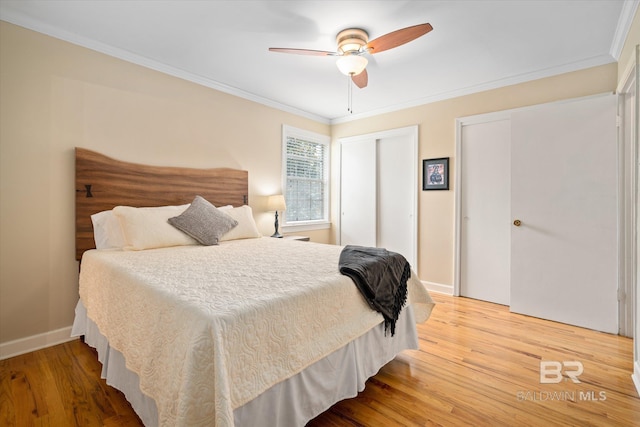 bedroom featuring baseboards, ornamental molding, wood finished floors, and multiple closets