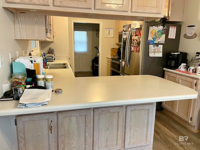 kitchen with appliances with stainless steel finishes, sink, wood-type flooring, kitchen peninsula, and light brown cabinetry