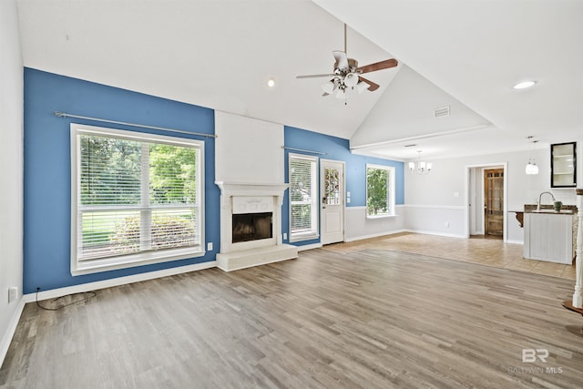 unfurnished living room featuring ceiling fan with notable chandelier, light hardwood / wood-style floors, high vaulted ceiling, and sink