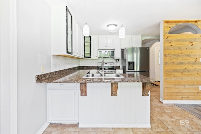 kitchen with white cabinetry, stainless steel appliances, backsplash, dark stone countertops, and decorative light fixtures