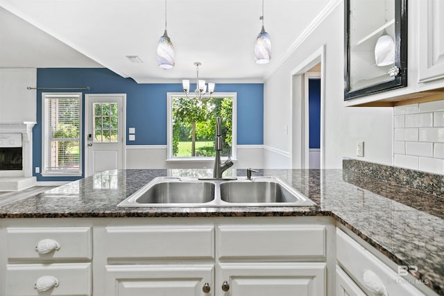 kitchen featuring dark stone counters, sink, white cabinets, and hanging light fixtures