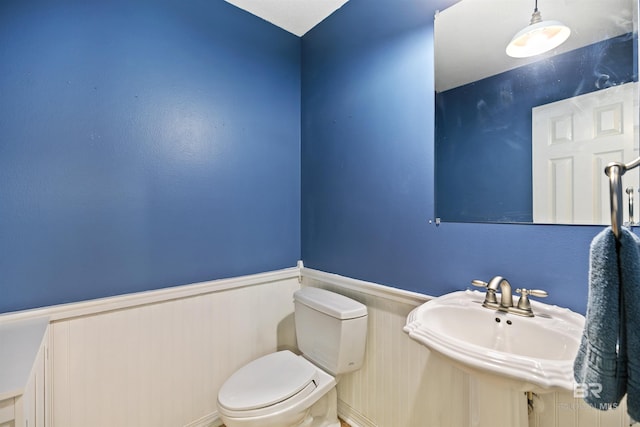 bathroom with toilet, wooden walls, and sink