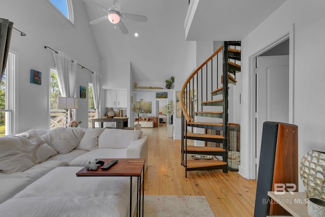 living room with a towering ceiling, light hardwood / wood-style floors, and ceiling fan