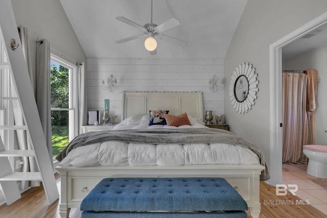 bedroom featuring ceiling fan, light hardwood / wood-style floors, wooden walls, and vaulted ceiling