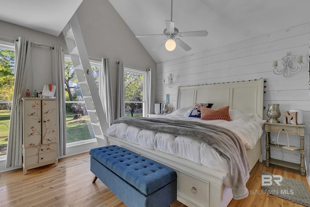 bedroom with light hardwood / wood-style flooring, vaulted ceiling, ceiling fan, and wooden walls