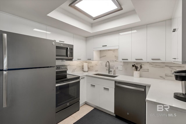 kitchen with tasteful backsplash, white cabinets, a raised ceiling, appliances with stainless steel finishes, and a sink