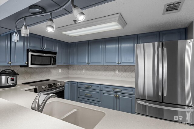 kitchen with stainless steel appliances, sink, blue cabinetry, and decorative backsplash