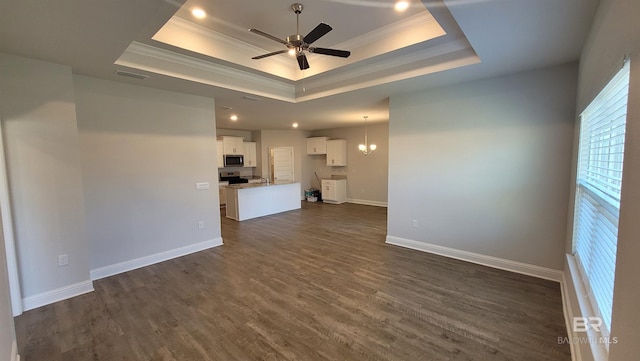 unfurnished living room featuring a raised ceiling, ornamental molding, ceiling fan with notable chandelier, and dark hardwood / wood-style flooring