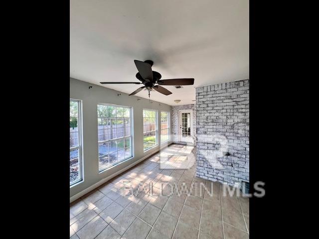 unfurnished living room with light tile patterned floors, brick wall, and ceiling fan