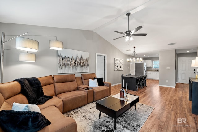 living room featuring baseboards, light wood finished floors, ceiling fan with notable chandelier, and lofted ceiling