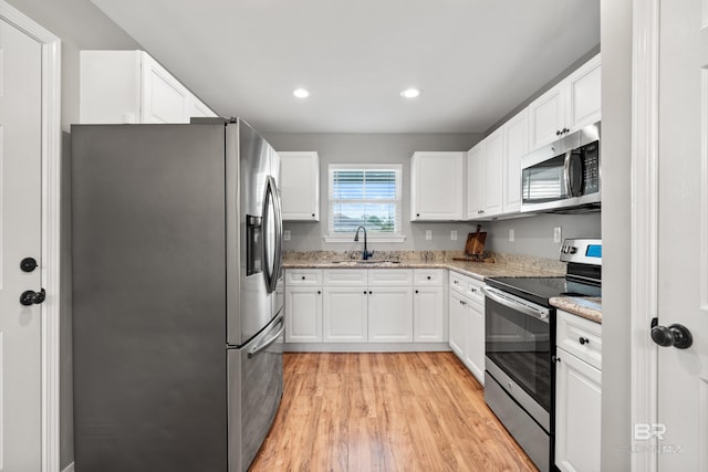 kitchen featuring white cabinets, light stone counters, a sink, stainless steel appliances, and light wood-type flooring