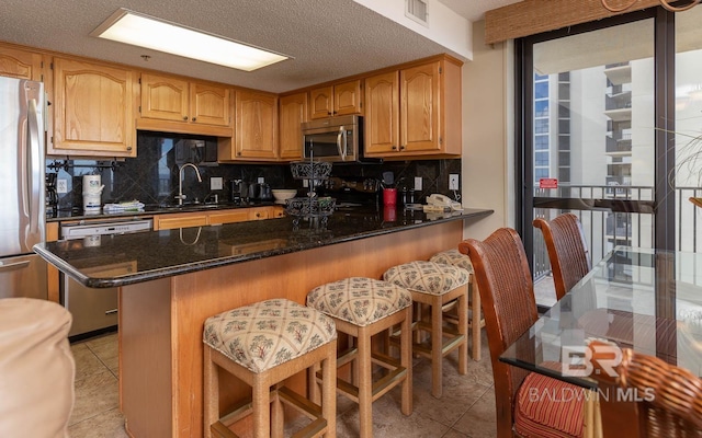 kitchen featuring decorative backsplash, a kitchen breakfast bar, stainless steel appliances, dark stone countertops, and light tile patterned flooring