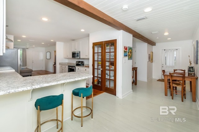 kitchen with appliances with stainless steel finishes, beam ceiling, white cabinetry, light stone countertops, and kitchen peninsula