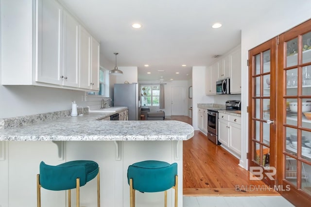 kitchen featuring kitchen peninsula, stainless steel appliances, light hardwood / wood-style floors, and a kitchen bar