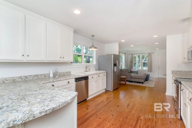 kitchen featuring appliances with stainless steel finishes, pendant lighting, white cabinetry, light stone countertops, and light hardwood / wood-style flooring