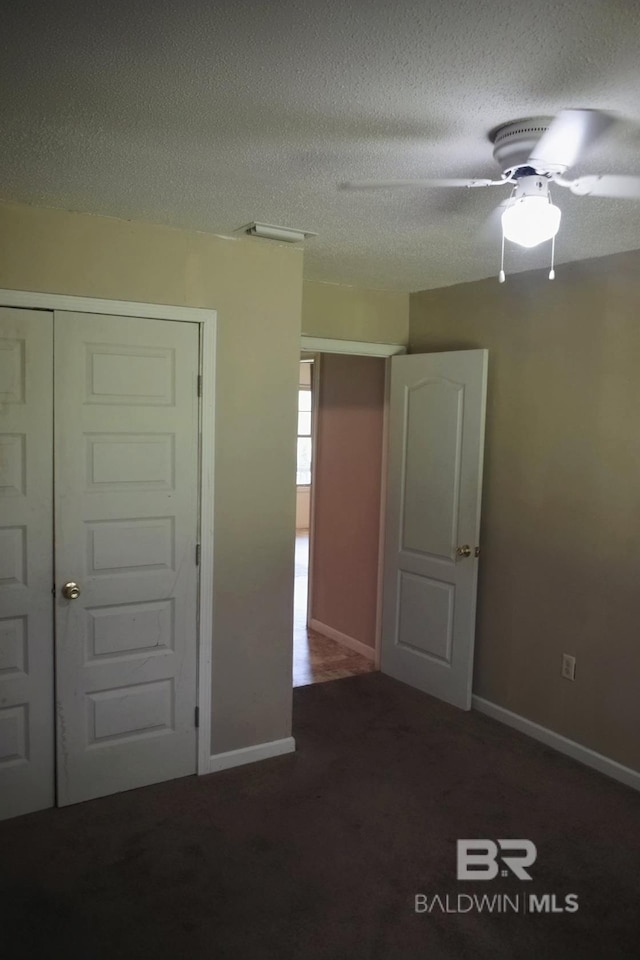 unfurnished bedroom featuring ceiling fan, a closet, a textured ceiling, and dark carpet