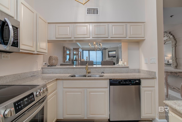 kitchen with light stone counters, sink, stainless steel appliances, and an inviting chandelier