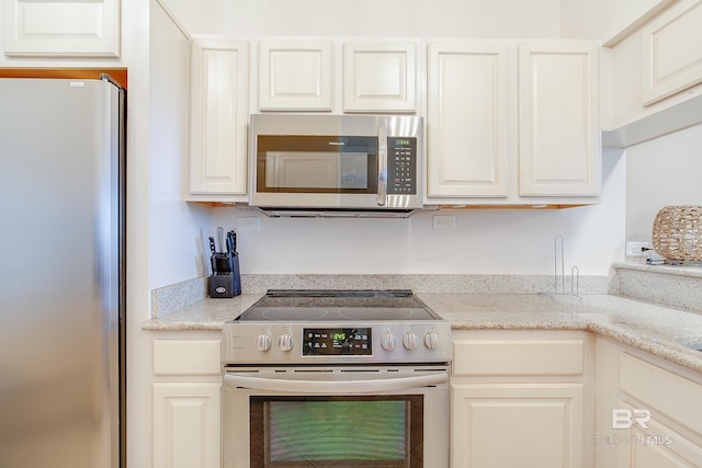 kitchen with appliances with stainless steel finishes, white cabinetry, and light stone counters