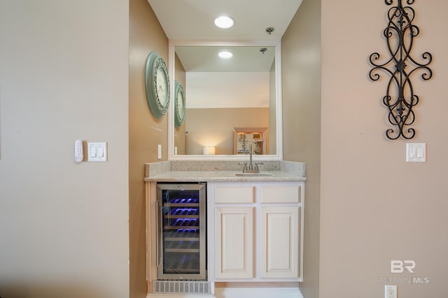 bar featuring white cabinets, light stone countertops, sink, and beverage cooler