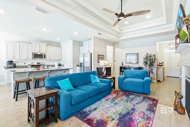 living room with ornamental molding, ceiling fan, a tray ceiling, and light hardwood / wood-style flooring