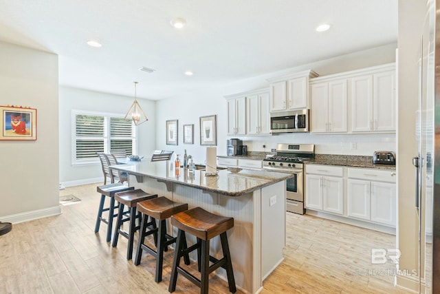 kitchen with an island with sink, light wood-type flooring, white cabinetry, appliances with stainless steel finishes, and a kitchen breakfast bar