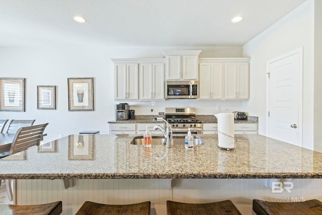 kitchen featuring light stone counters, white cabinets, a spacious island, appliances with stainless steel finishes, and a kitchen breakfast bar