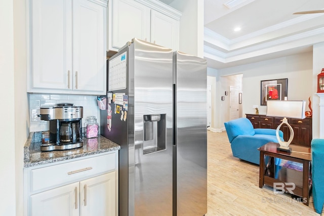 kitchen with light wood-type flooring, decorative backsplash, white cabinets, stainless steel fridge, and dark stone countertops