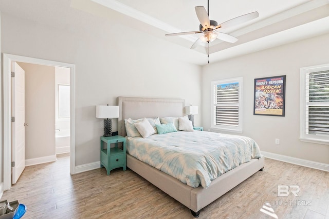 bedroom with light wood-type flooring, ceiling fan, crown molding, ensuite bath, and a tray ceiling