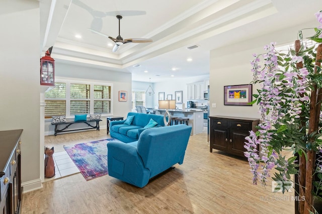 living room with ceiling fan, ornamental molding, light hardwood / wood-style flooring, and a tray ceiling