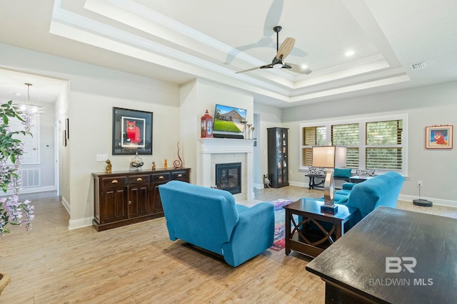 living room featuring ceiling fan with notable chandelier, a raised ceiling, a fireplace, and light hardwood / wood-style floors